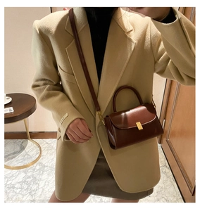 Detail of a dark brown leather crossbody bag featuring a golden buckle and slim strap
