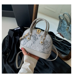 Detail of embroidered floral shell bag with golden hardware and leather base trim