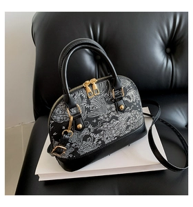 Detail of black shell bag featuring white traditional patterns and gold hardware on leather