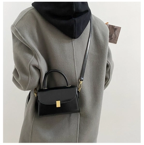 Detail of a black matte square bag with gold buckle on a grey coat in casual style