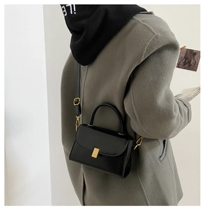 Close-up of minimalist black leather crossbody bag with golden metal buckle clasp