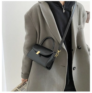 Detail of a black leather square bag with gold buckle on a model in a grey blazer