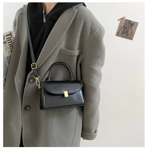 Detail of a black leather square crossbody bag with gold buckle on a grey coat