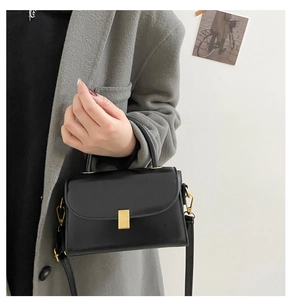 Detail of elegant black leather crossbody bag with a minimalist gold rectangular lock