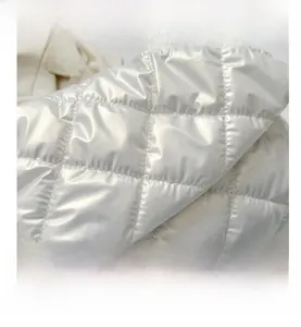 Gros plan sur un tissu matelassé blanc cassé avec motif losange et fini nacré