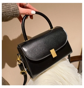 Close-up of black glossy leather bag with gold rectangular clasp and fine glitter detail