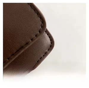 Close-up of litchi grain leather texture and precise stitching on dark brown crossbody bag