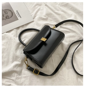 Detail of black matte leather square bag with gold metal buckle on white background