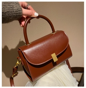 Detail of vintage brown leather handbag featuring a metallic buckle and long strap