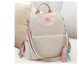 Détail d'un sac à dos en nylon beige avec finitions roses et breloque pompon colorée