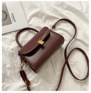 Detail shot of a dark brown crossbody bag with gold metal buckle on a white fabric background
