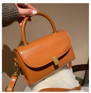 Detail of orange-brown leather small square bag with matte gold rectangular buckle closure