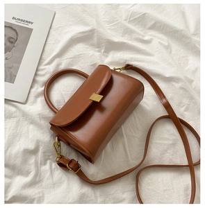 Detailed top view of a brown leather small square bag with gold buckle on white fabric