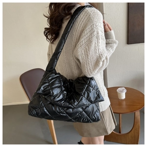 Détail d'un sac bandoulière matelassé noir brillant porté par un mannequin en pull