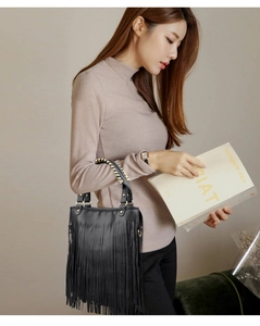 Close-up of black lychee leather bag with long tassels and woven chain strap