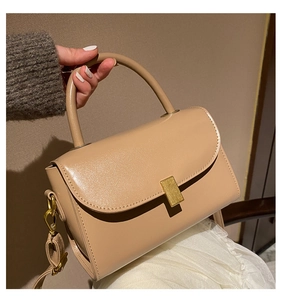 Detail of warm beige leather handbag featuring a sleek gold rectangular metal clasp buckle