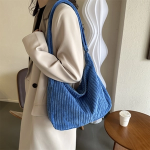 Detail of blue corduroy hobo tote bag texture showing crossbody fit on soft beige blazer