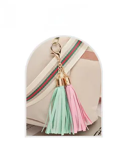 Détail d'un pendentif à glands rose et vert avec fermoir mousqueton doré sur un sac beige