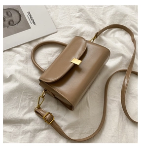 Top view of a caramel leather crossbody bag with a gold buckle on white fabric