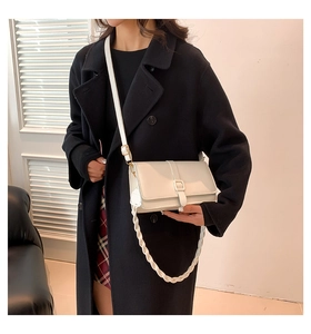 Detail view of cream square crossbody bag with textured woven strap on black coat