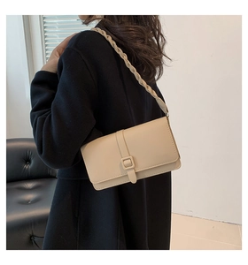 Detail of cream shoulder bag featuring woven strap and square buckle on model