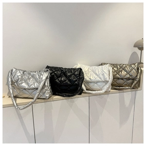 Sacs bandoulière matelassés en argent, noir, blanc et bronze disposés sur un bureau en bois