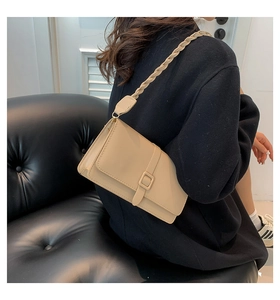 Close-up of beige faux leather shoulder bag featuring a decorative buckle and woven strap
