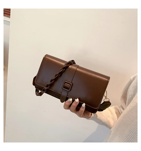 Detail of dark brown leather square bag with woven handle and metallic hook hardware