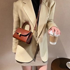 Brown leather square crossbody bag with gold T-clasp shown in a casual street style