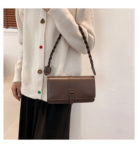 Detail of dark brown matte leather bag with stylish braided shoulder strap worn on shoulder