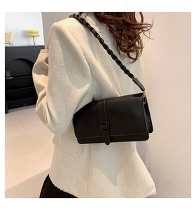 Detail of a vintage black rectangular flap bag featuring a unique spiral woven shoulder strap