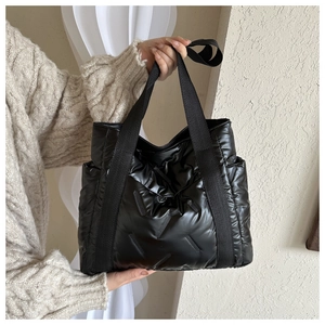 Detail of black quilted puffer tote bag with glossy finish and wide webbing handles