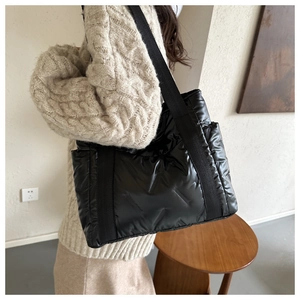 Detail of black quilted puffer tote bag with glossy nylon finish and wide fabric straps
