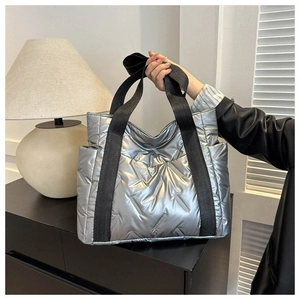 Close-up of silver quilted puffer tote bag with black nylon straps and side pockets