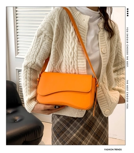 Close-up of bright orange shoulder bag with unique wavy flap and adjustable strap details