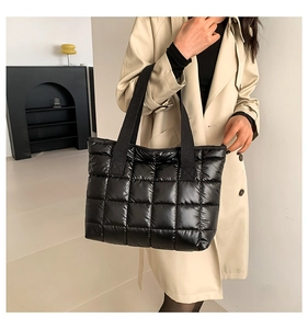 Detail of a black quilted puffer tote bag in glossy nylon worn with a beige trench coat