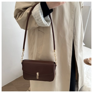 Detail of dark brown vintage shoulder bag with gold clasp on a beige trench coat