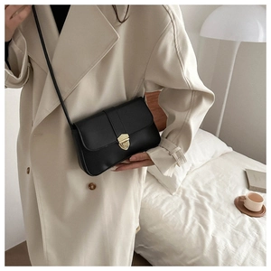 Close-up of black leather crossbody bag with gold buckle on a model in trench coat