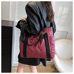 Detail of burgundy quilted tote bag with metallic nylon texture and wide black shoulder strap