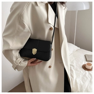 Close-up of a black leather crossbody bag with a gold shield-shaped lock on a trench coat