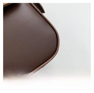 Detailed close-up of brown leather texture and stitching on minimalist shoulder bag