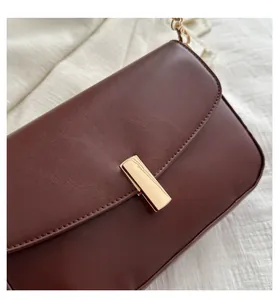 Detail of dark brown leather handbag with gold metal clasp and fine stitching accents