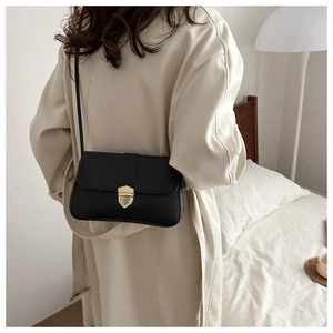 Lifestyle shot of a black minimalist crossbody bag with gold shield buckle on a beige trench coat