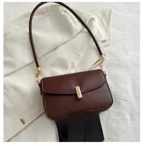 Detail view of dark brown leather flap bag with gold clasp shown next to a smartphone