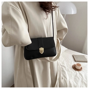 Minimalist black rectangle shoulder bag with gold shield buckle on woman in beige coat