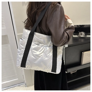 Silberne Stepp-Tote-Bag mit V-Muster und schwarzem Gurt in Büro-Umgebung gezeigt