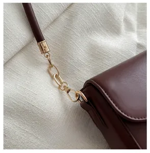 Detail shot of the golden metal lobster clasp and chain link on a leather shoulder bag