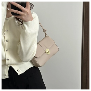 Close-up of minimalist beige shoulder bag featuring a gold triangle metal buckle and knot strap