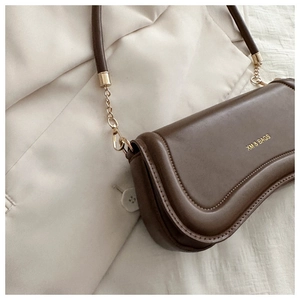 Detail of dark brown leather shoulder bag with gold chain strap on beige clothing
