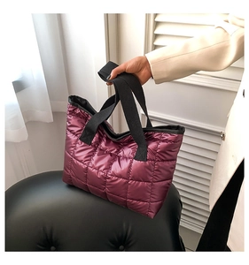 Detail of purple quilted puffer tote bag with black straps held by model in white suit